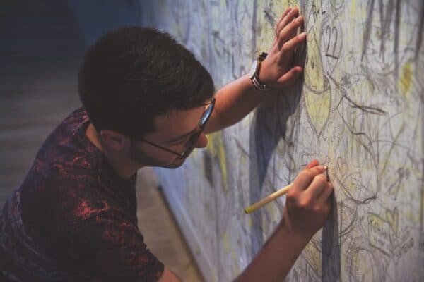壁に鉛筆で絵を描く男性